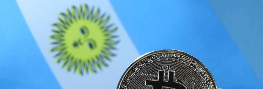 Image of part of the Argentina flag with a bitcoin representation in front of it.
