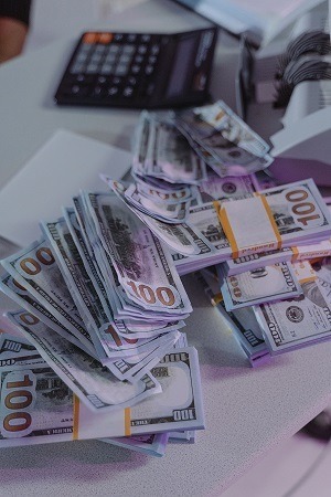 Image of U.S. currency piled on a table with a calculator in the background.