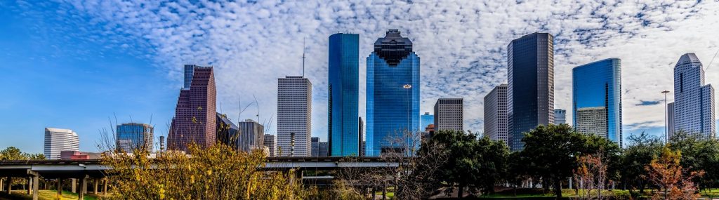 Image of the Houston Texas skyline with blue skies and light clouds in the background.