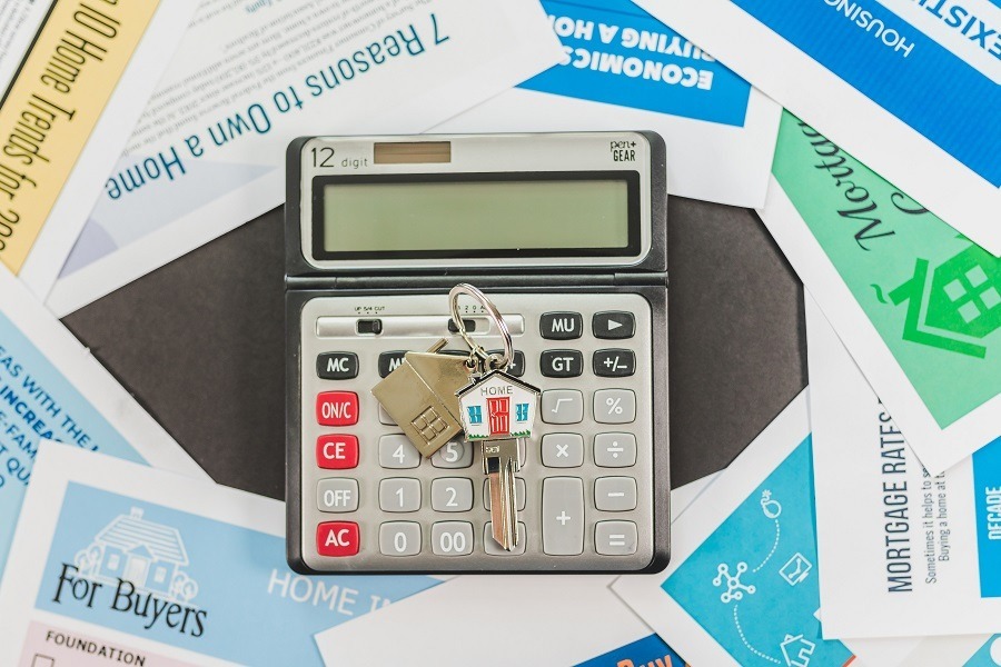 Image of a calculator sitting on a pile of paperwork with a house key.