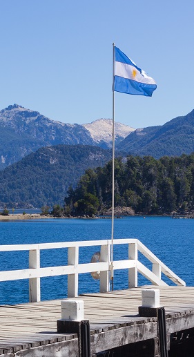 image of a flag on a dock near large body of water and mountains in the background