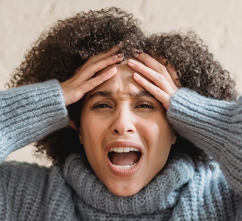 A visibly upset person with their hands pulling their hair back.