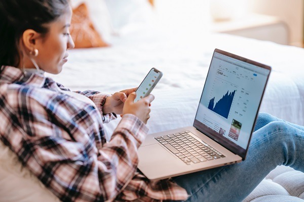 Person sitting on a couch looking at a smart phone and a laptop computer at the same time