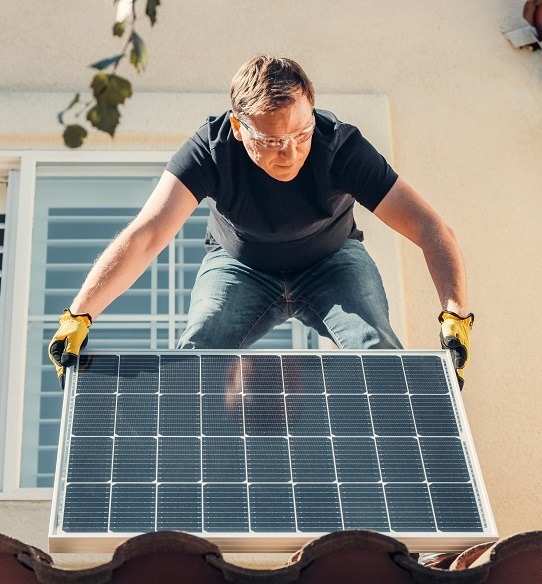 A person installing a solar panel on a house roof.