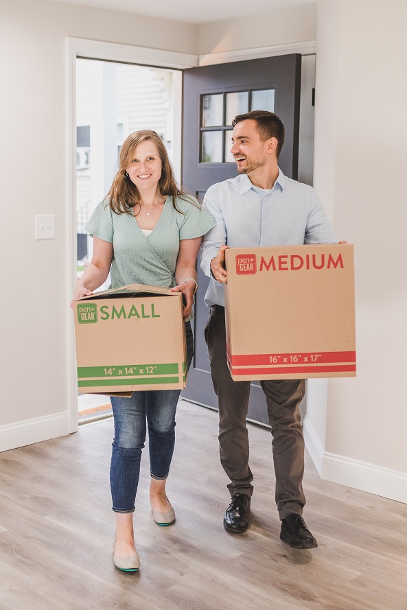 Two people standing in a house holding moving boxes.