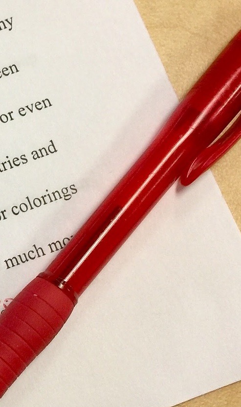 Viewing the corner of a real estate deed laying on a table. There is a red correction ink pen on top of the document and errors in the document have been noted.