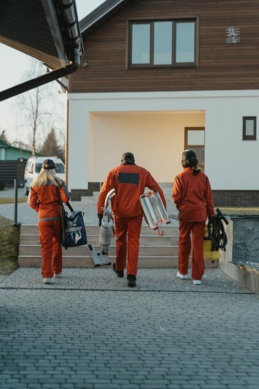 People walking up stairs to a house carrying tools