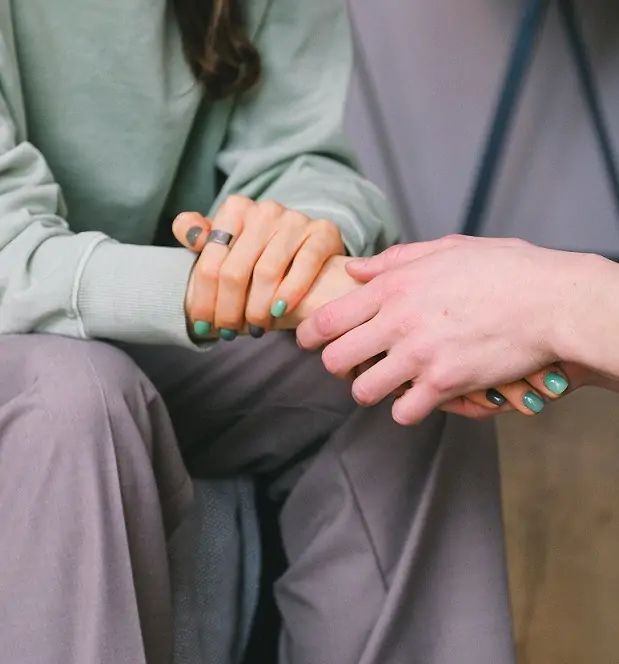 Two people sitting, holding hands, consoling each other.