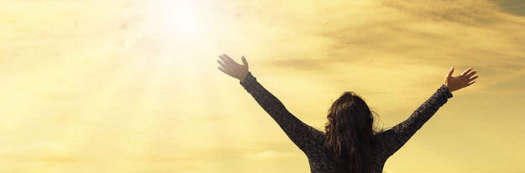 A person with their arms outstretched towards the sun happy that their mortgage is paid off.