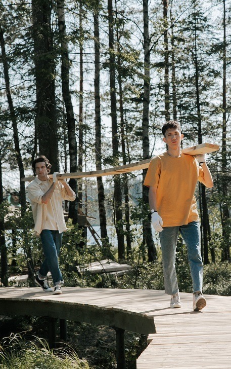 Two people walking outside carrying a piece of lumber