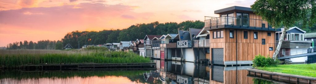 Image of several houses near a body of water with the sun setting n the background.