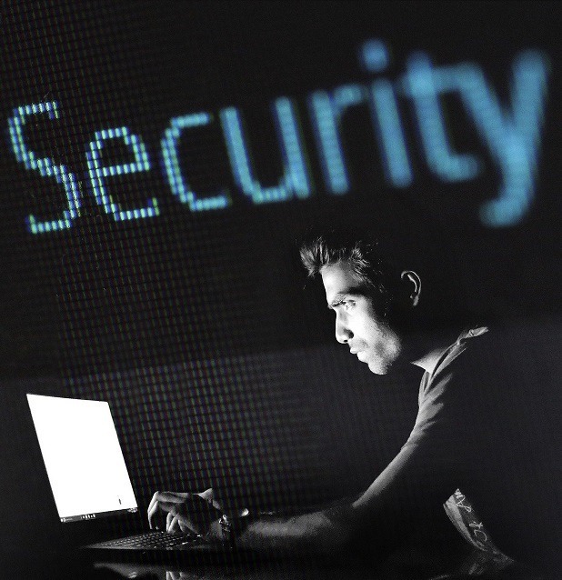 Person working in a computer in a dark scene with a large illuminated security sign behind them.