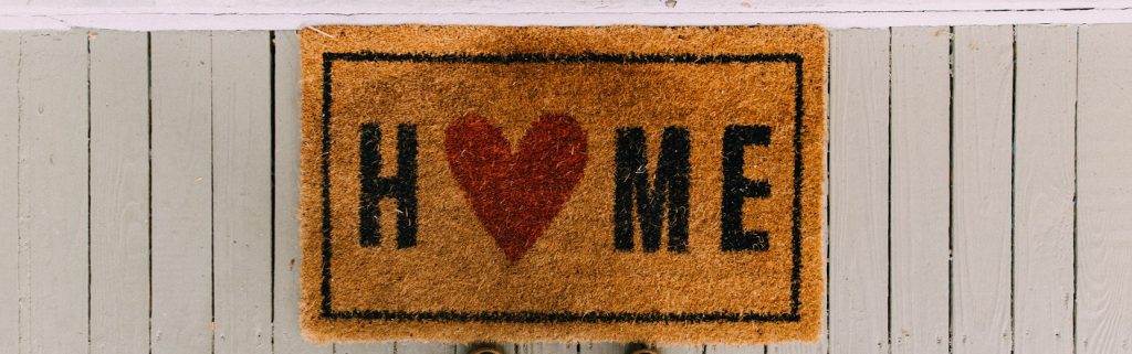 Image of a doormat that says "home" sitting at the front door of a house.