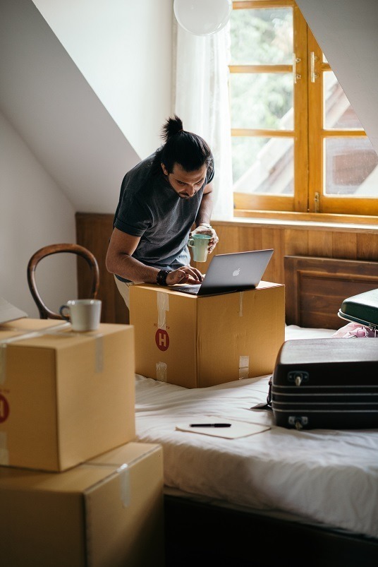 Person looking at a computer in a house with moving boxes around them.